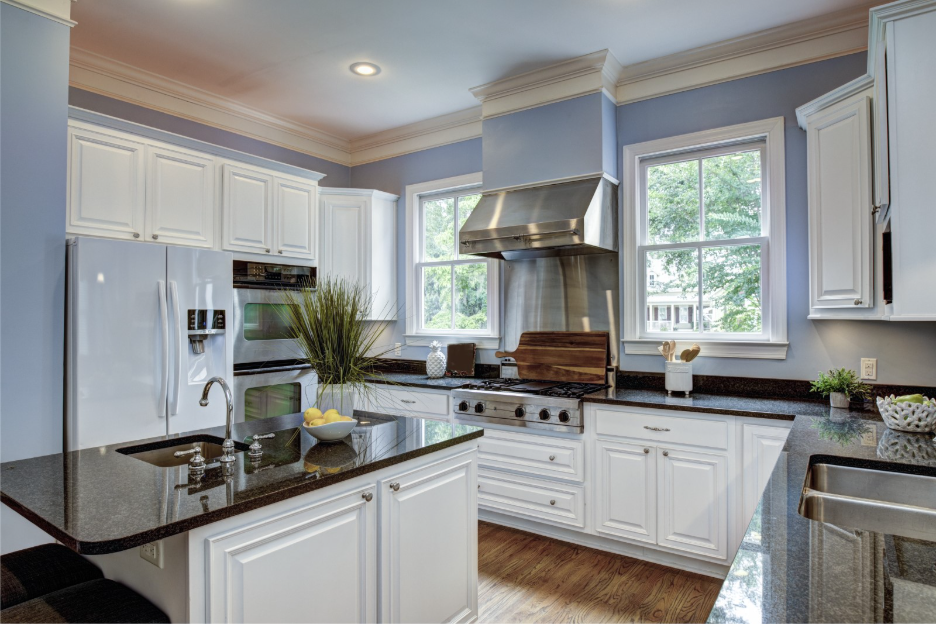 Bright kitchen with white cabinetry, dark granite countertops, a large island, stainless steel appliances, and blue walls.